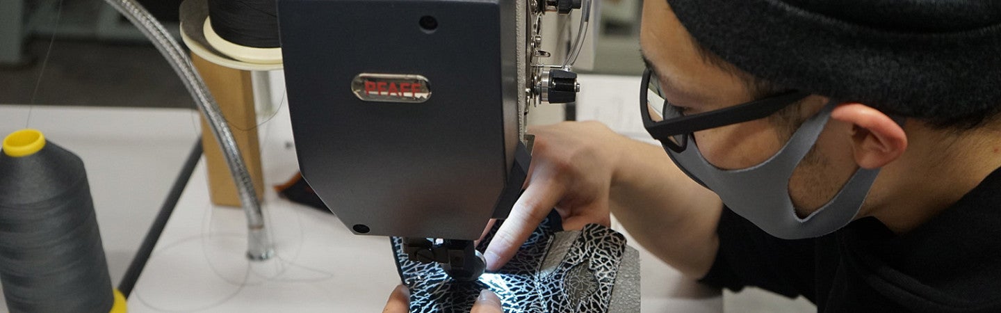 Close up on SPM student Yoshimi Saito as he uses an industrial sewing machine to make a shoe in the SPM lab