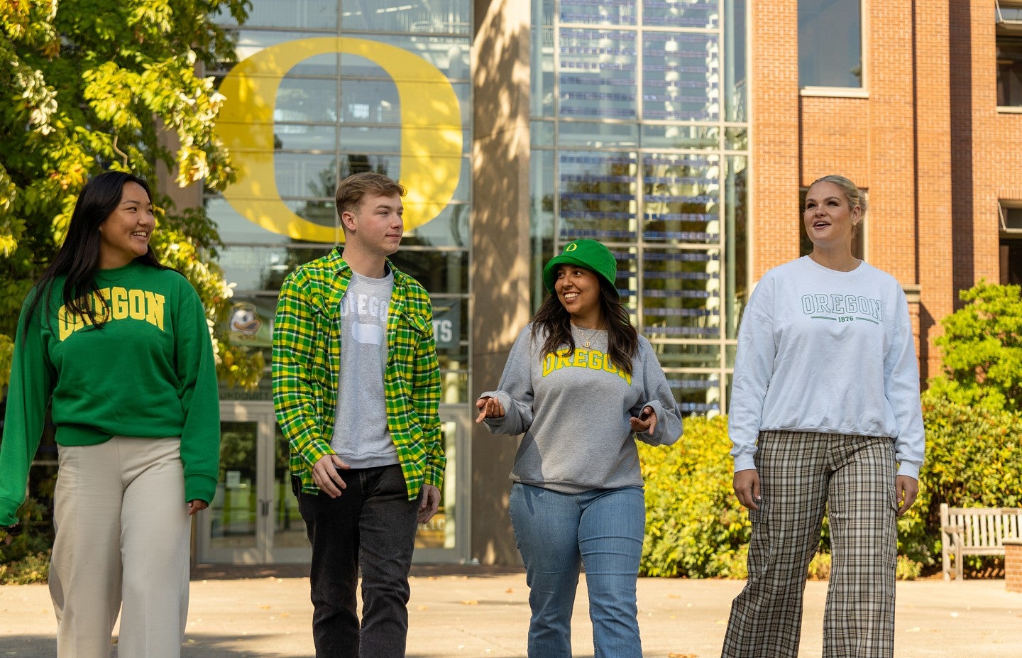 A small group of students walking outside towards the camera in front of the Lillis Business Complex and talking to each other.