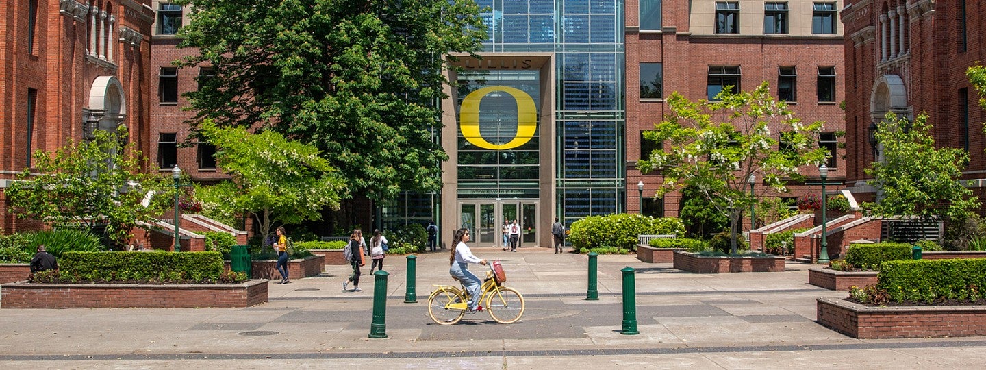 Outside view of the Lillis Business Complex with a student riding a yellow bike in front of the building.