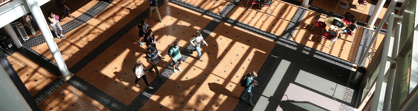 Students walking through the Lillis Business Complex atrium with a large O shadow on the floor.