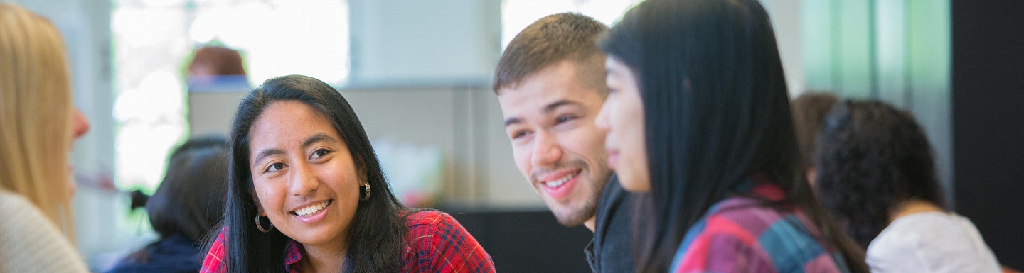 Student sitting at a table, talking and looking at papers on the table.