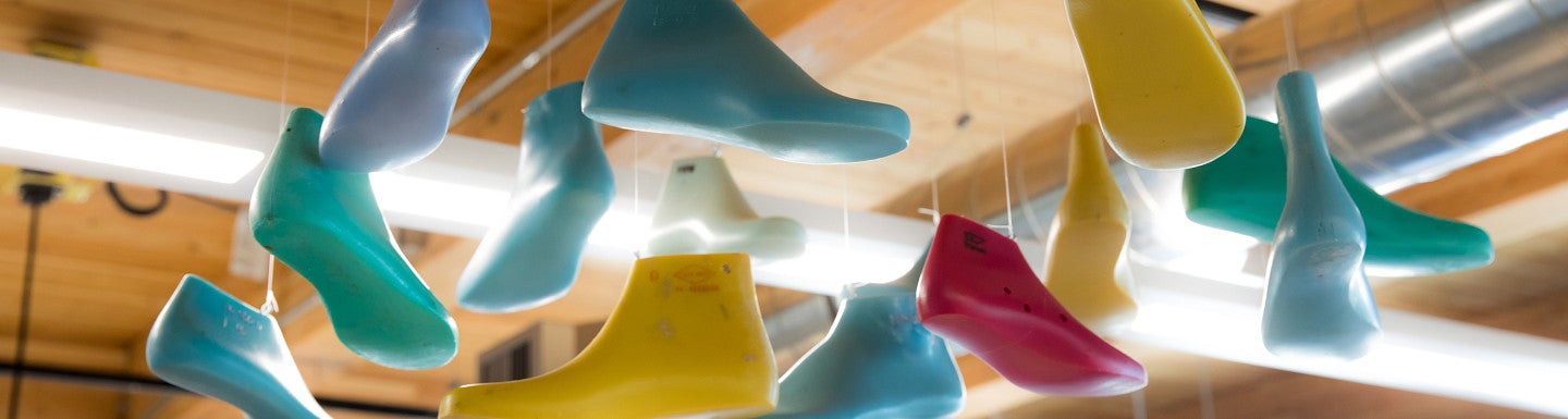 Multiple different-colored shoe molds hanging from a wooden ceiling