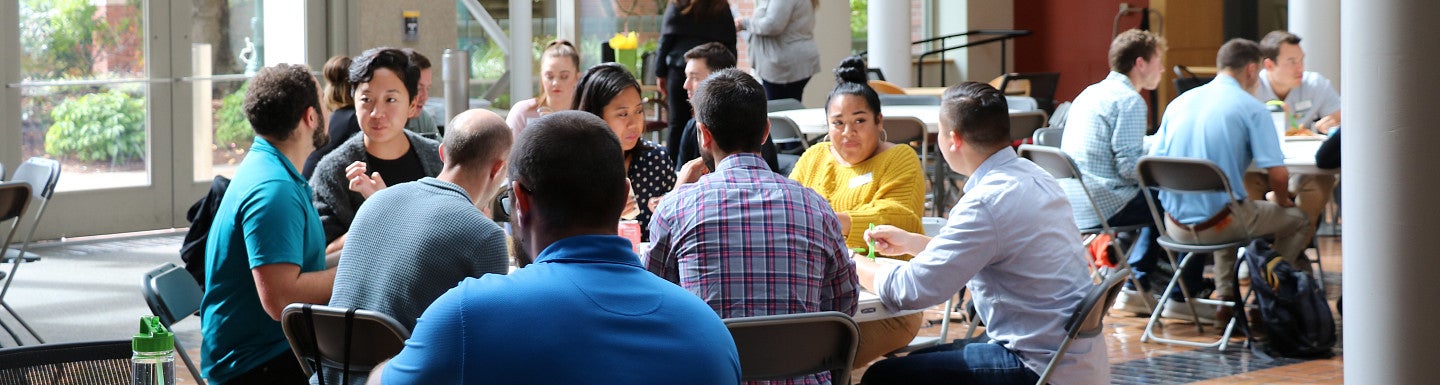 Several students sitting at large round tables and chatting in the Lillis Business Complex atrium