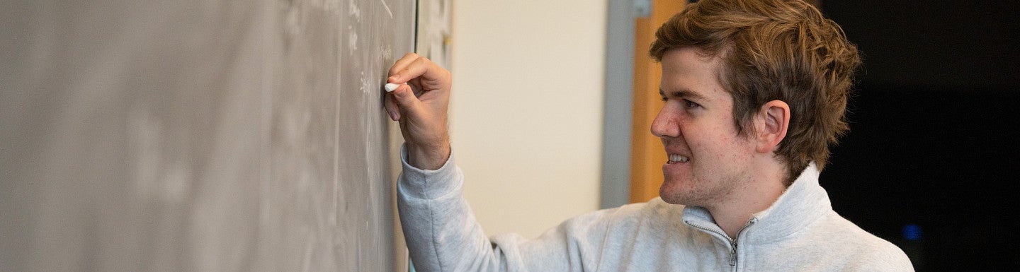 Student standing at a chalkboard smiling and writing