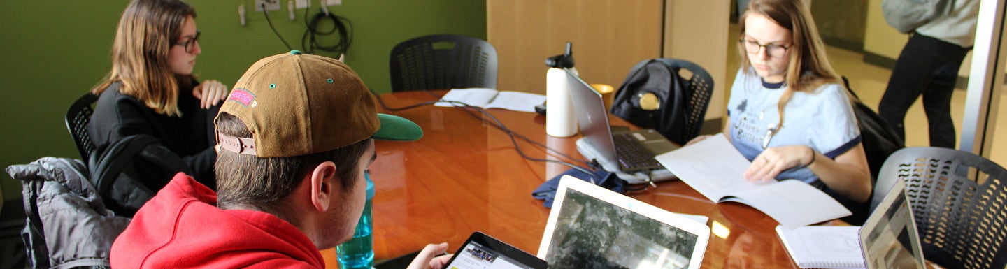 Students sitting at a table with laptops working on a project.