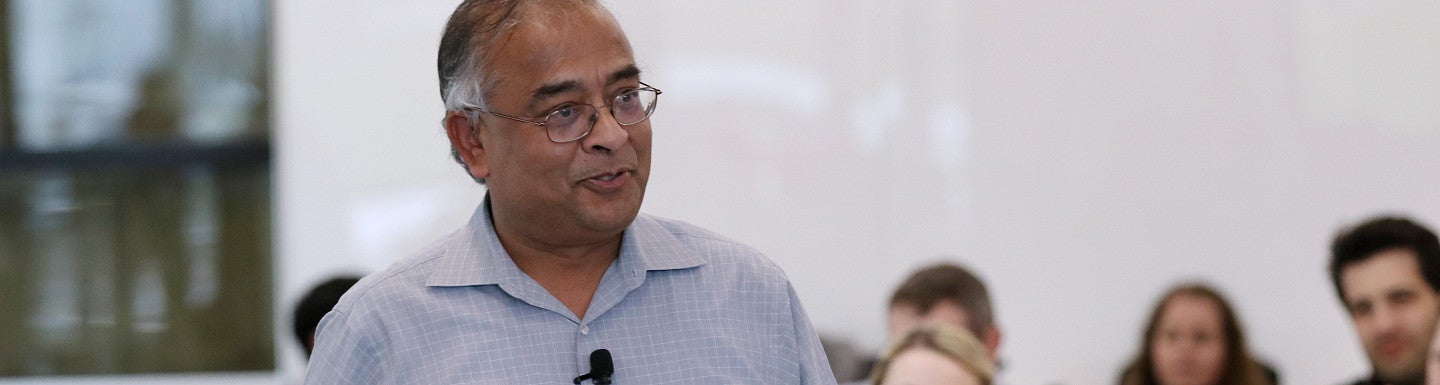 Male professor standing in front of a class of students, smiling and talking