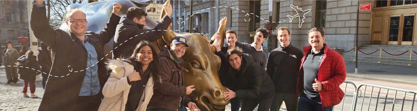 A group of MBA students pose for a photo around the Wall Street bull statue