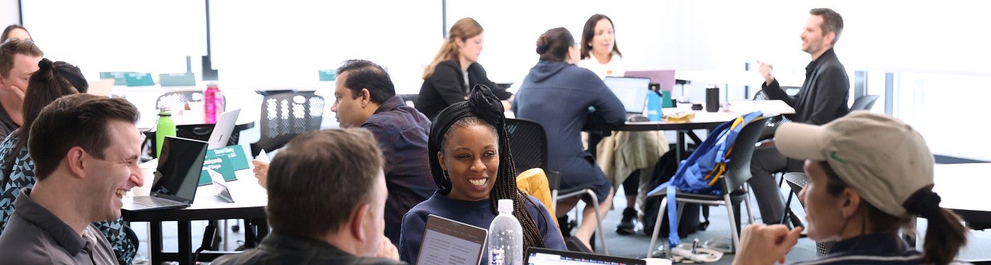 Classroom full of students sitting at tables talking and laughing while working on projects.