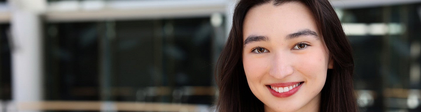 Young woman smiles. She has long black hair and is wearing a black and white sweater with gold buttons. 