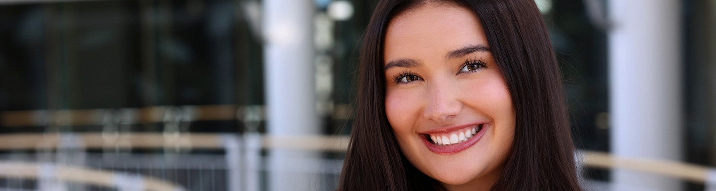 Young woman smiles at the camera. She has long dark hair and is wearing a black blazer and black shirt.