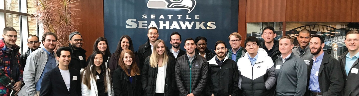 MBA students take a group photo in front of the Seattle Seahawks logo