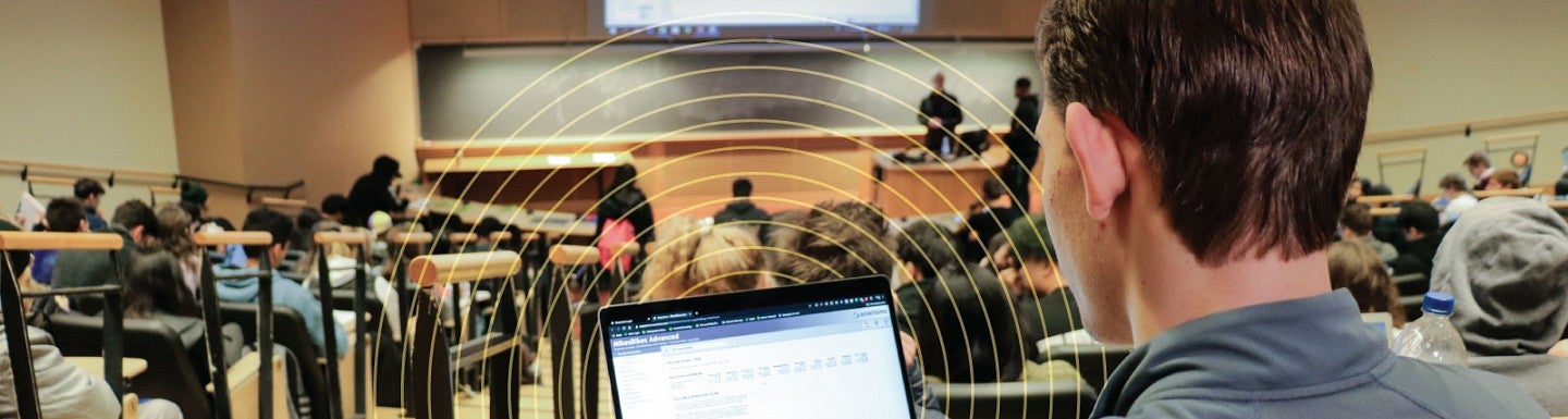 A student takes notes on his laptop during class in a large auditorium