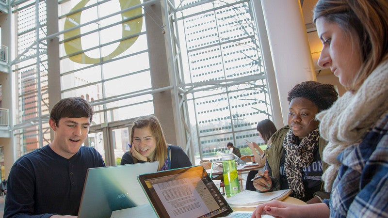 A group of students with laptops working together in the Lillis Business Complex.