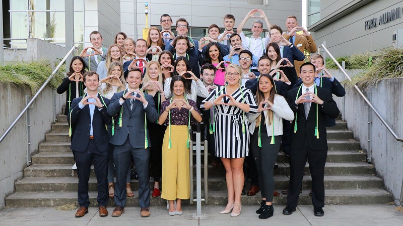 A group photo of business honors students standing on the steps of the Ford Alumni Center and holding their hands in an O shape..