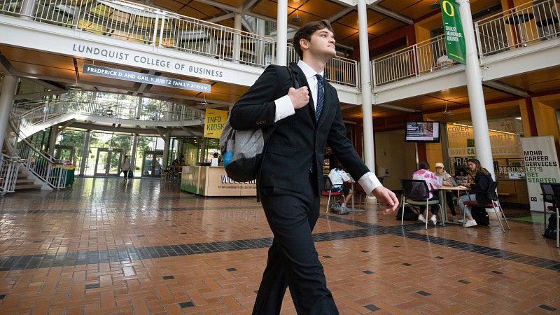 One student wearing a suit and carrying a backpack walking through the Lillis Complex atrium
