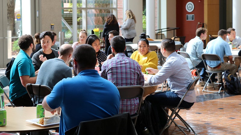 Several students sitting at large round tables and chatting in the Lillis Business Complex atrium