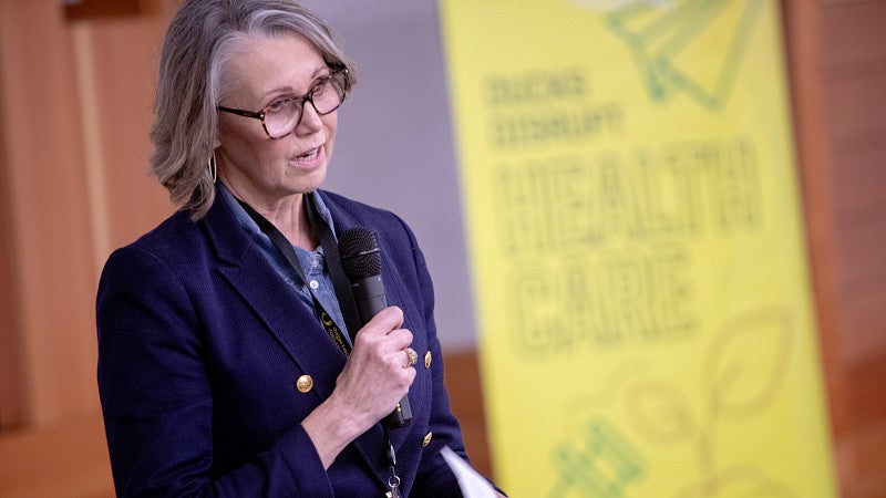 Event speaker standing with a microphone talking, with a yellow floor banner in the background