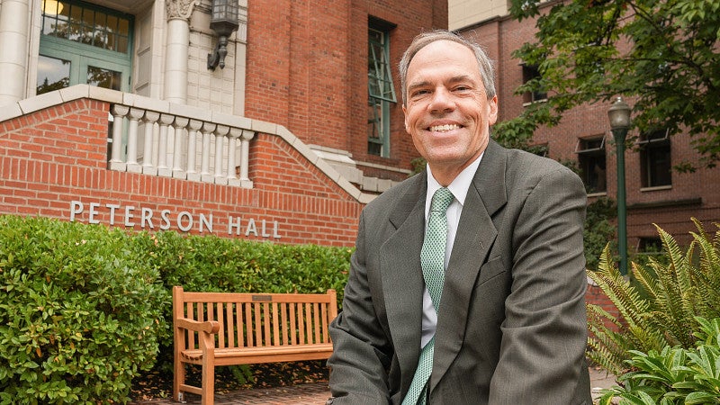 Bruce Blonigen sitting on the edge of a planter with Peterson Hall in the background