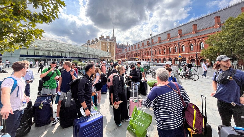 This candid shot depicts a group of MBA students gathered with their luggage on the streets of Paris on a sunny day.