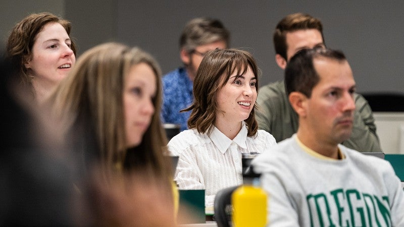 Close-up of six students sitting in a tiered classroom looking forward. One student is smiling while the rest are concentrating.