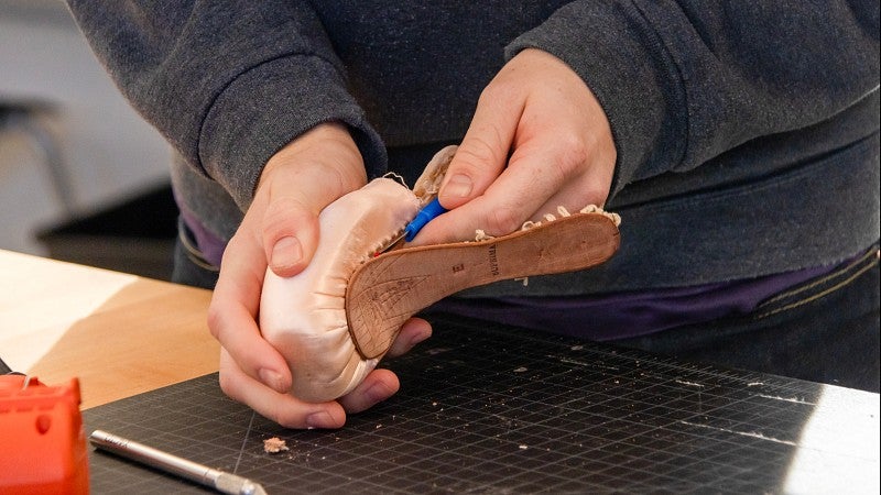 A close-up of a student's hands working with tools on a shoe mold.