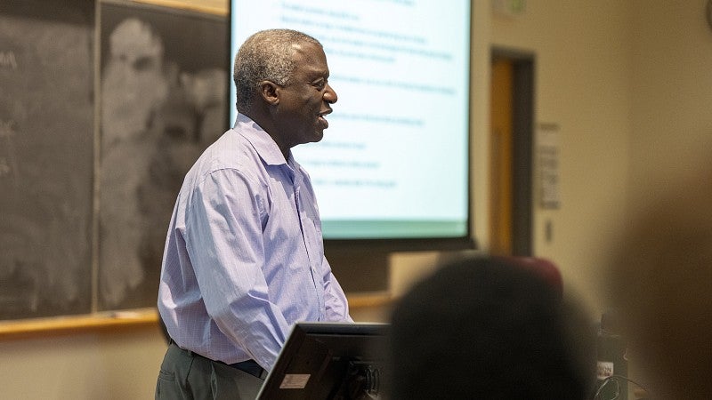 A close-up photo of a faculty member standing and talking in the front of a classroom.