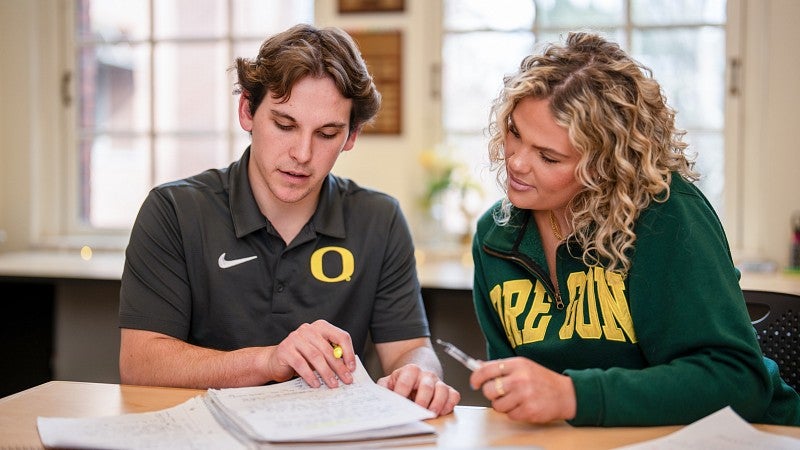 Two students sitting next to each other looking through a notebook.