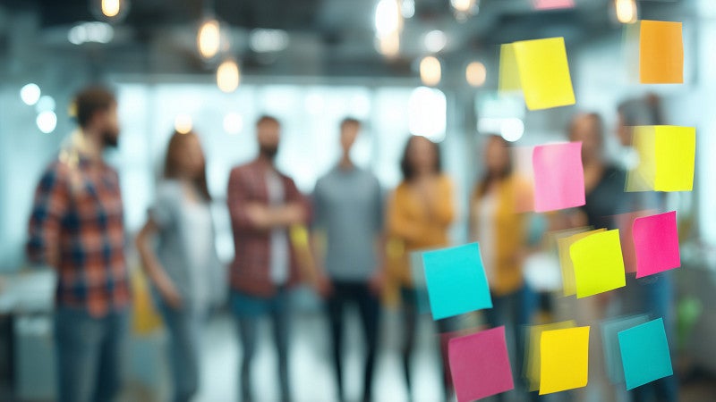 A group of people in the background standing behind a window with sticky notes on it.