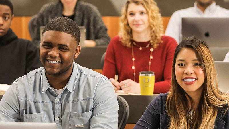 Sports Product Management students in class facing the camera and smiling in response to a professors point