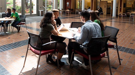 Group of students sitting at a table in the Lillis Business Complex atrium collaborating on a project.