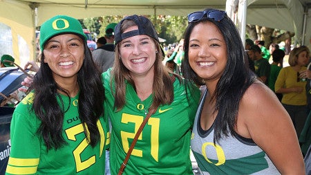 Three students smiling at a University of Oregon tailgate event.