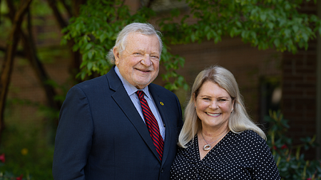 Photo of Chuck and Gwen Lillis smiling while looking at the camera in front of a green bush on the University of Oregon campus