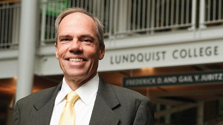 Head shot photo of Bruce Blonigen standing in front the the Lundquist College of Business sign in the Lillis Business Complex atrium
