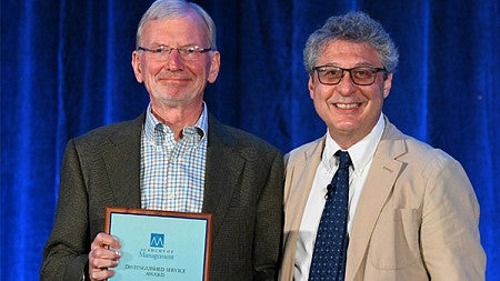 Alan Meyer holds up his lifetime achievement award while posing for a photo at the AOM conference