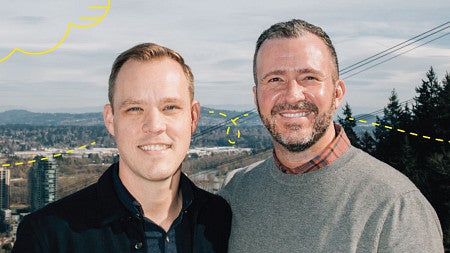 Photo of Banning Hendriks, MBA ’19, (left) and his husband Chris Hamel (right) looking at the camera and smiling with the Portland, Oregon, skyline behind them.