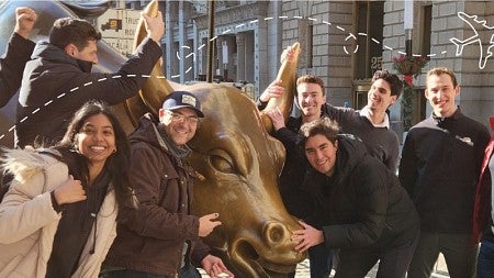 A group of MBA students pose for a photo around the Wall Street bull statue