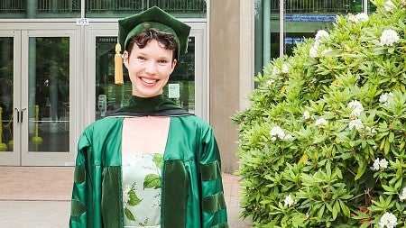 PhD graduate Sophie Pychlau wearing her commencement regalia in the courtyard outside the Lillis Business Complex