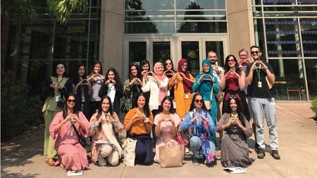 Group photo of Pakistani women and their hosts, making the "O" symbol with their hands in front of the southern entrance to the Lillis Business Complex