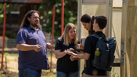 MBA students talk amongst themselves as they take notes outside of a greenhouse