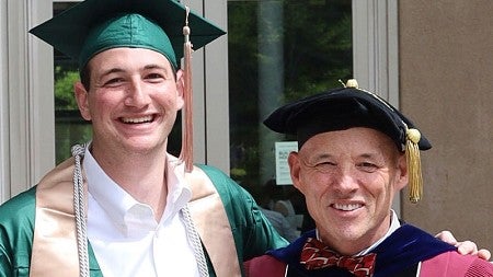 Adam Kovar and Charlie Bame-Aldred, both wearing commencement regalia