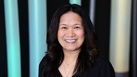 Profile head and shoulders photo of Jinky Panganiban smiling at the camera with parted long black hair standing in front of light tubes in lobby of 109 Naito