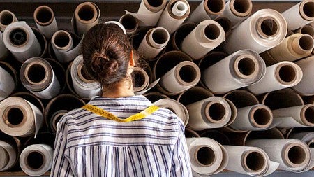 A women standing in front of a wall of fabric roles of different sizes contemplating the implications of her choice.