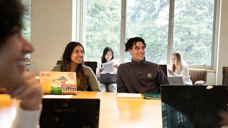 Students sit together in a study area and listen to a presenter who is not seen