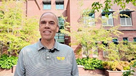 Screenshot of a video with Dean Bruce Blonigen standing outside the Lillis Business Complex on a sunny day