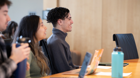 Three students sitting around a long table watching a live presenter