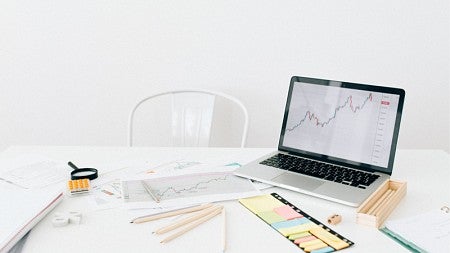 A desk upon which a laptop, post-it notes, printouts of a graph, a calculator, pencils, and other office supplies have been placed.