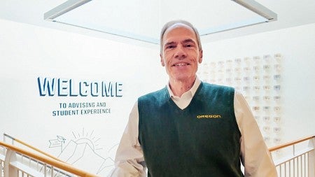 Lundquist College dean Bruce Blonigen stands in front of wall art in the Lillis Business Complex that includes the text "Welcome to Advising and Student Experience"