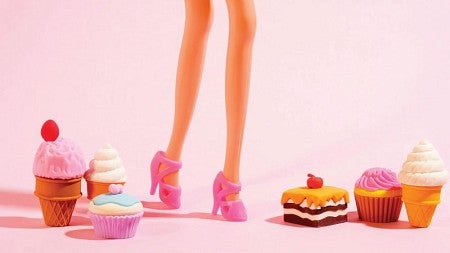 A Barbie doll, seen from the knees down, stands amongst several toy treats set around its feet