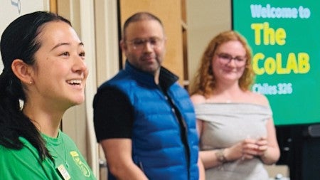 Photo from the opening of the CoLab showing a smiling women student looking sideways toward the audiencein the foreground with CoLAB banner behind her 