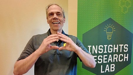 Dean Bruce Blonigen makes the -O- symbol with his hands as he stands in front of a sign for the Insights Research Lab